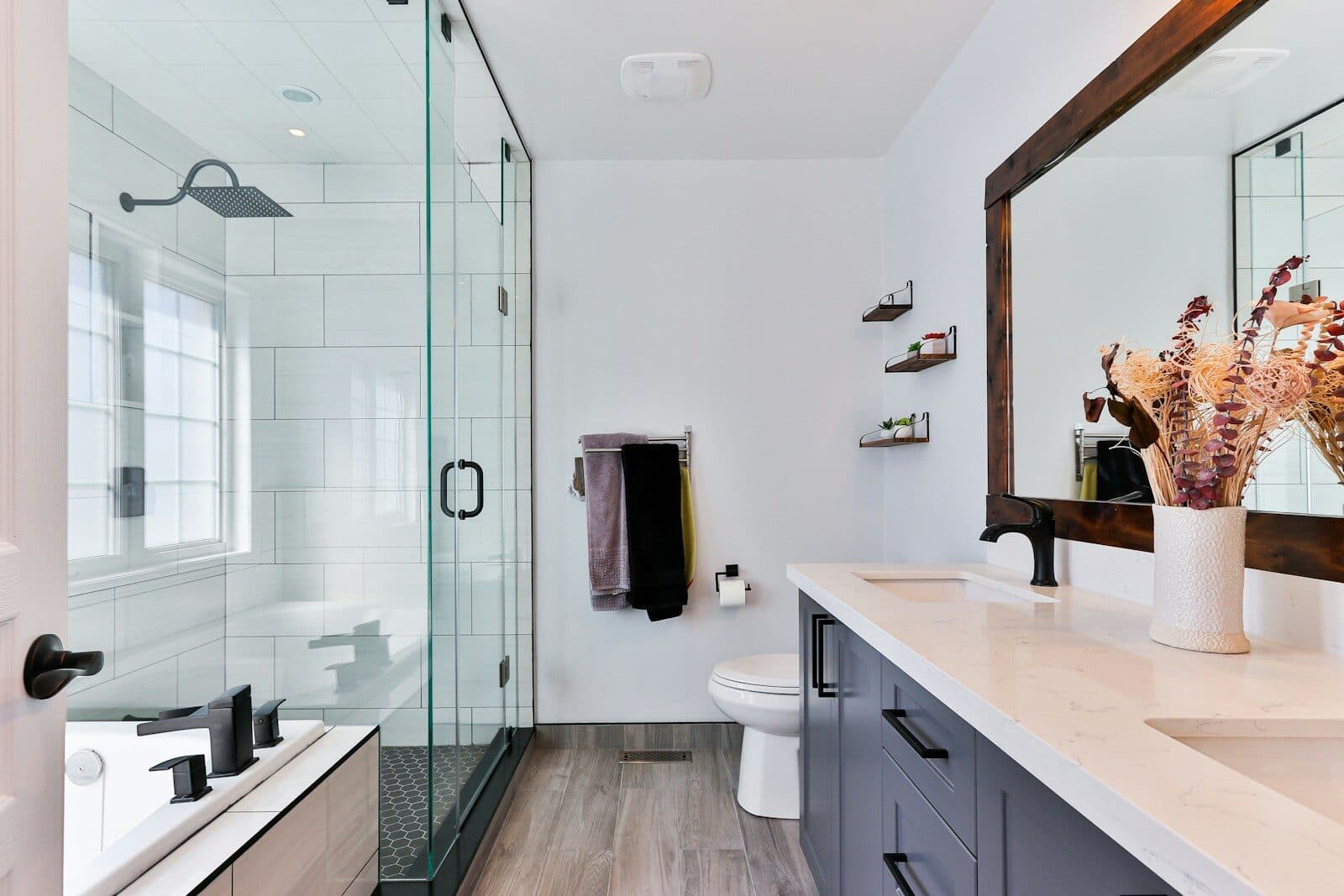A finished bathroom with a tiled walk-in shower behind a glass screen, a vanity unit and a wood floor