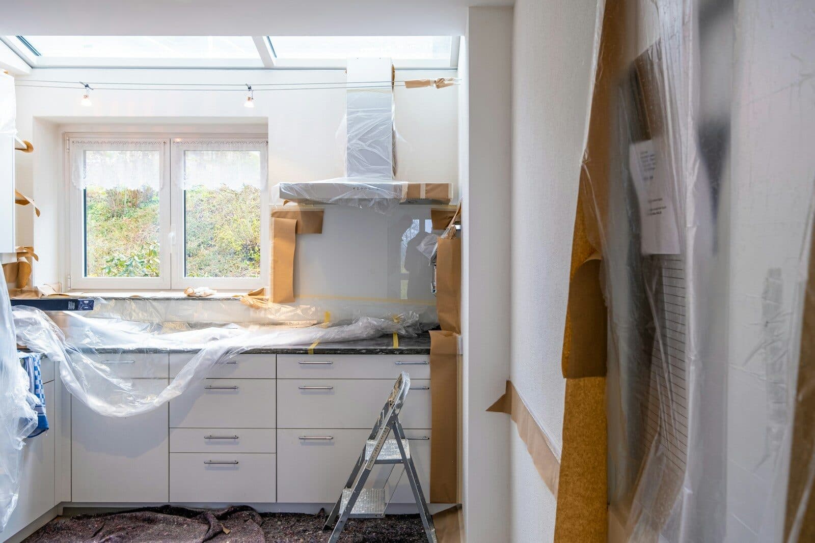 A kitchen part-way through a renovation, units covered in dust sheets with a stepladder in the room