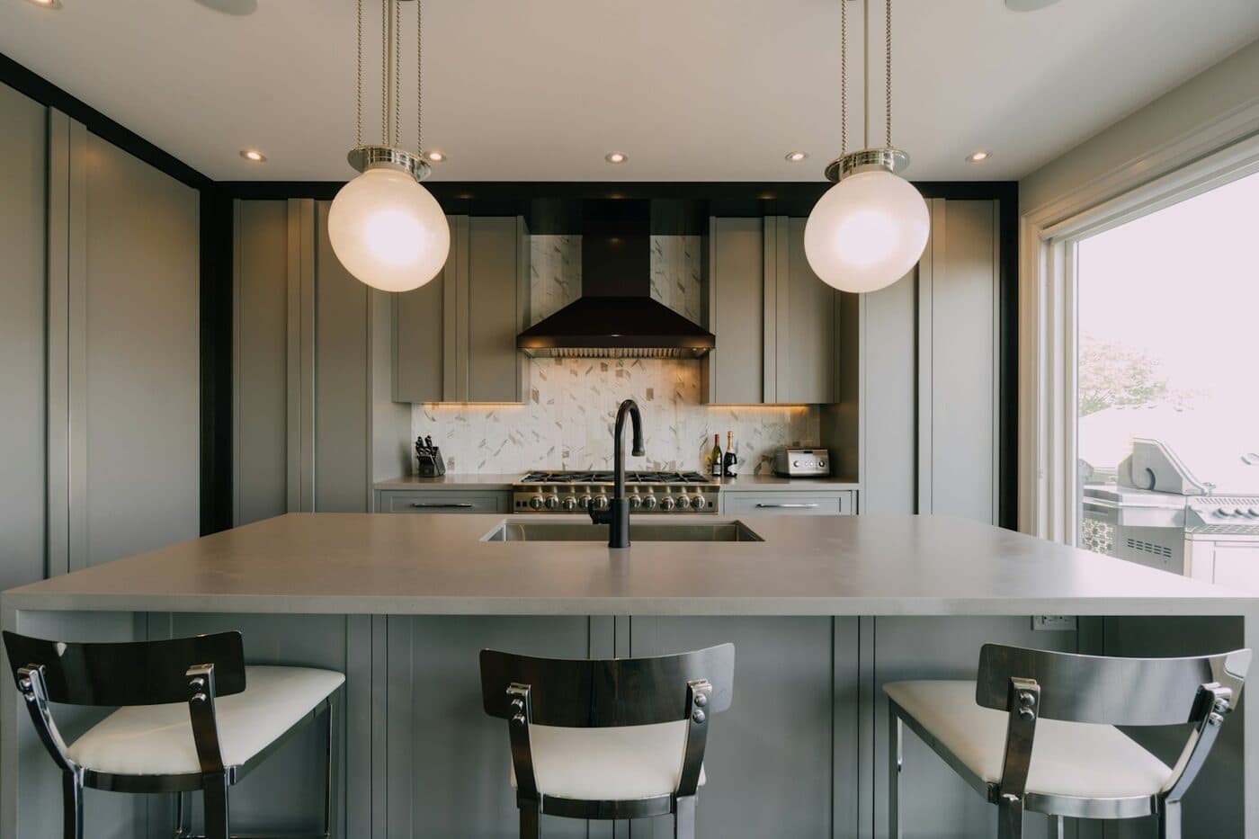 A kitchen with dark green painted narrow-frame doors, a pale worktop and pendant lights over an island